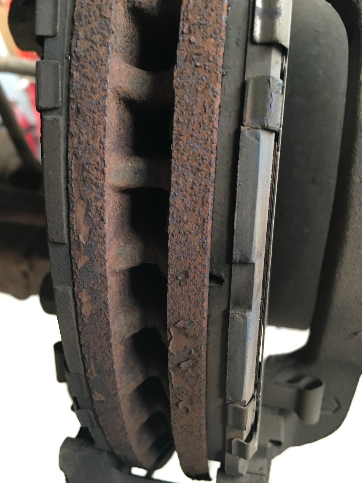Heavily corroded brake disc and pads still on the car, before replacement